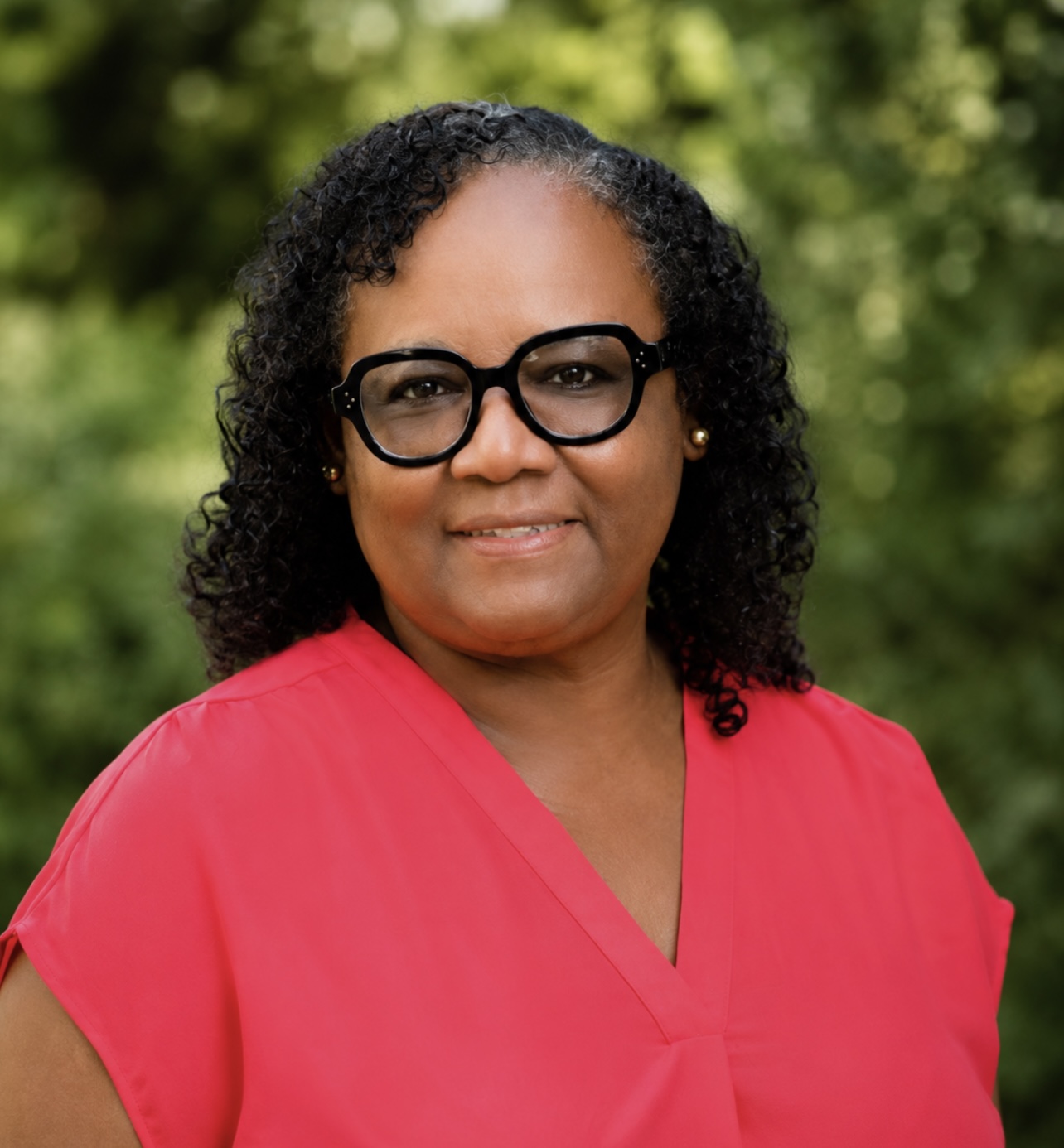 Women with black hair and glasses smiling at the camera. She is wearing a salmon shirt