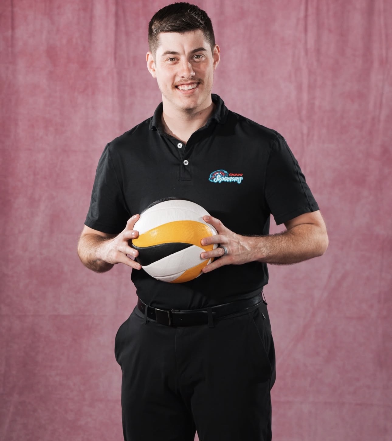 White man in a black polo shirt holding a volleyball