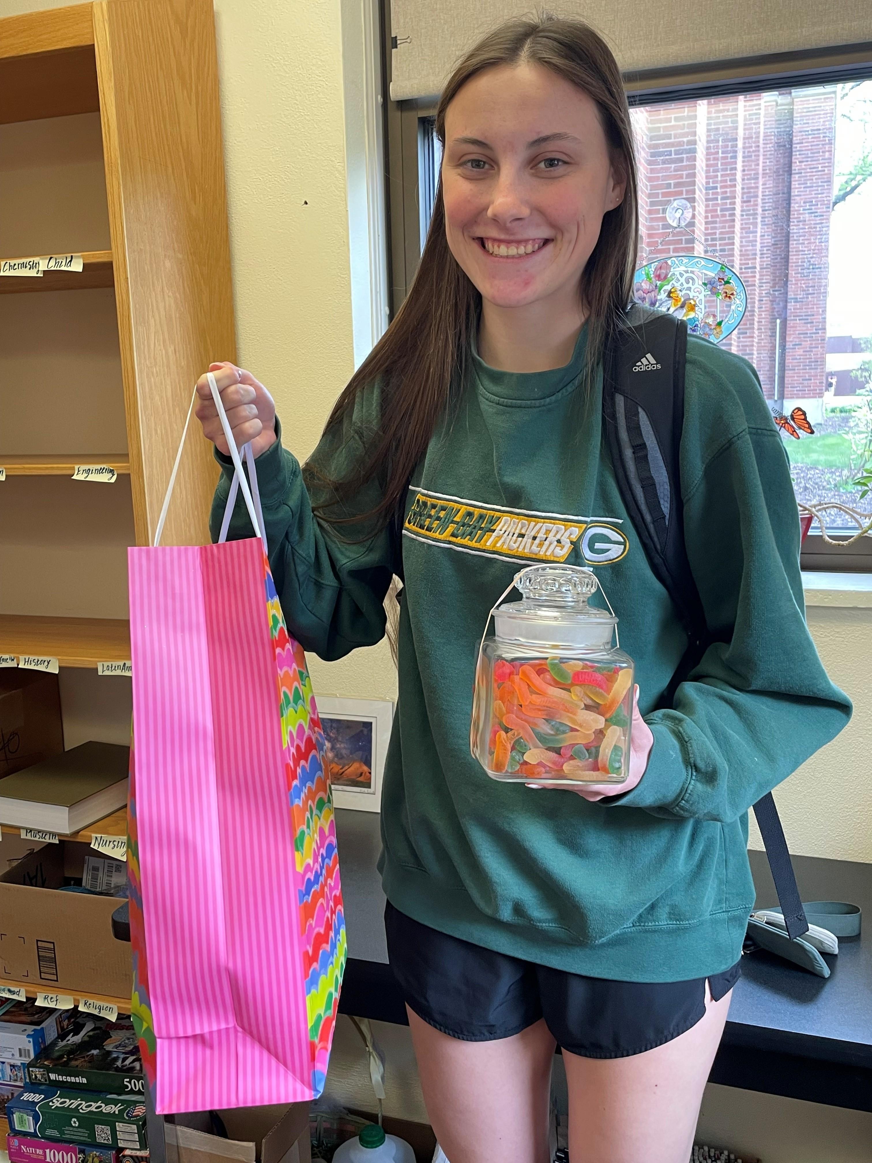 Photo of a young woman holding a gift bag and a glass jar of colorful gummy worms.