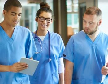 Two male and one female nurse with a stethoscope on looking at an iPad.