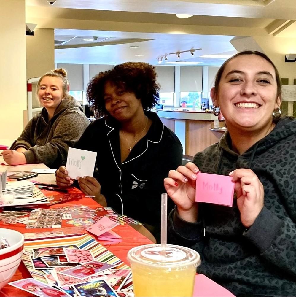 Three smiling female students show off the valentine's cards they've made